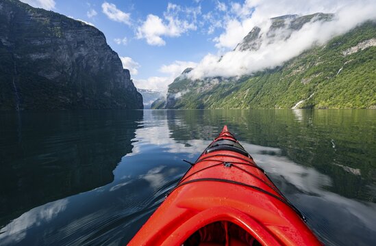 Kayak trip on the Geirangerfjord, tip of a red kayak in the fjord with reflection, atmospheric fjord landscape, first person view at Geiranger, M&oslash;re og Romsdal, Norway
