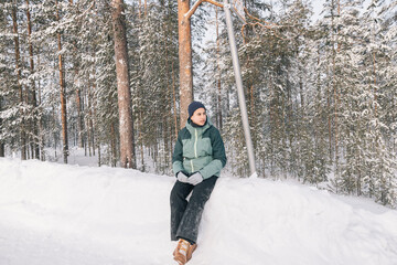Naklejka premium Teenager girl wearing winter clothes sitting and relaxing in a snowy forest, enjoying the peace and quiet of nature