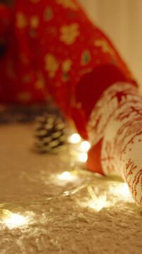 Vertical video. Close Up of Festive Sock with String Lights and Decorated Tree in Background on Soft Carpet in Warm Room
