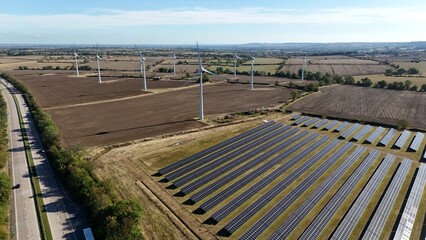 Aerial drone shot of wind turbine and solar panel photovoltaic power plant, generating renewable energy electricity in England UK