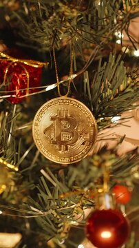Vertical video. Bitcoin Ornament Hanging on Decorated Christmas Tree with Lights, Berries, and Small Golden Gifts