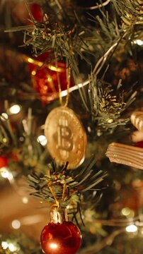 Vertical video. Bitcoin Ornament Hanging on Christmas Tree with Bow Paper Balls and Berries Illuminated by Soft Glow for a Digital Economy Celebration