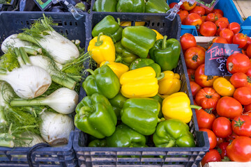 Fresh colorful vegetables at farmers market: green and yellow bell peppers, red tomatoes, and white fennel in plastic crates. Vibrant organic produce display.