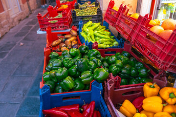 Vibrant display of fresh green bell peppers, colorful vegetables and produce arranged in red and blue plastic crates at traditional outdoor street market.