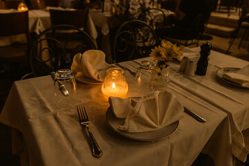 Intimate restaurant table beautifully set with glowing candles, yellow sunflowers, and elegant place settings creating perfect romantic dining atmosphere.