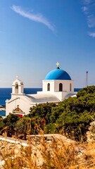 Obraz premium A picturesque whitewashed church with a vibrant blue dome stands proudly against a backdrop of a clear blue sky and the ocean.