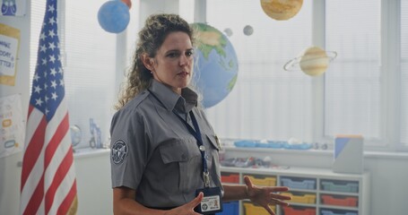 American Female Policewoman in Uniform Visiting Primary School Classroom, Giving Lecture to Curious Students About Safety Rules. Police Officer Teaching Children About Discipline, Law and Protection.