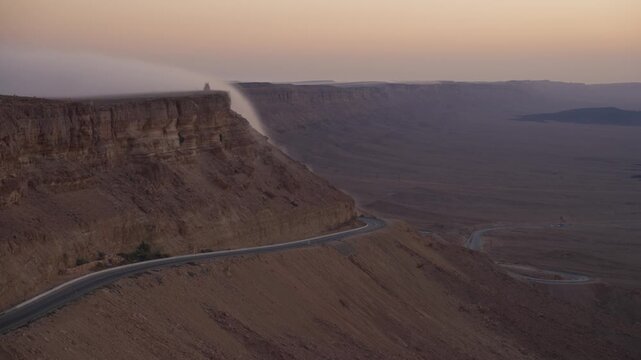 Beautiful desert mountain in early morning sunrise with cloud waterfall or fog in Mitzpe Ramon, Israel. Overlooking Ramon Crater. Arid dry terrain in colorful orange warm colors
