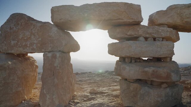 Sunlight beaming through a cairn, a man made arch of stacked stones, creating lens flare over vast desert landscape in stone park in Israel Negev desert overlooking Ramon Crater. Harmony and peace