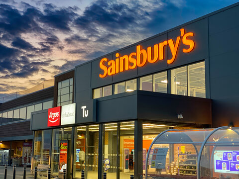 EPSOM, UK - AUGUST 22, 2025: Sainsbury's supermarket at dusk with Argos, Habitat, Tu signage, retail branding, urban commerce.