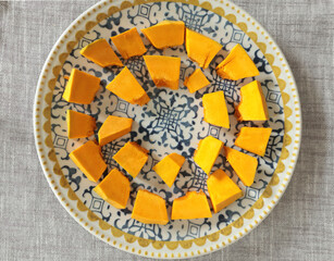 Pieces, cubes of pumpkin on porcelain plate with blue pattern. Farm products and healthy eating. Kitchen and home cooking.
