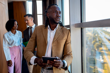 African American businessman with tablet looking through window while working in office.