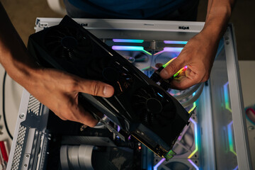 Computer technician installing new graphics card into modern custom-built pc with RGB lighting, enhancing gaming performance and visual experience. Stages of upgrading or assembling desktop computer