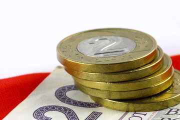 Stacked coins, each worth two Polish zlotys, are placed on a banknote. The colors of the Polish flag are white and red