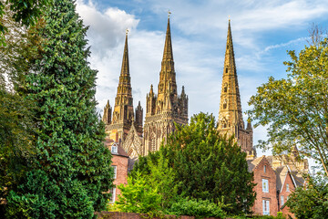 A view of the three spires of Lichfield Cathedral protruding above the trees in summertime