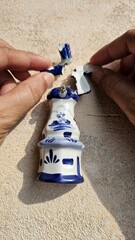 Hand is holding part of typical souvenir from the Netherlands, a windmill-shaped refrigerator sticker made of ceramic, damaged and broken due to falling, isolated on a beige background.