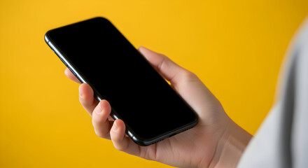 Hand holding a modern smartphone with a blank black screen against a vibrant yellow background, perfect for digital content