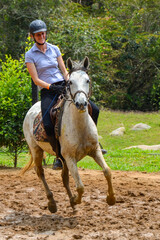 Woman riding a horse at a gallop on a sandy track in Colombia, smiling and enjoying the outdoor activity