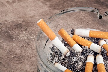 Hand putting cigarette in glass ashtray. Health concept.