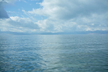 Vast expanse of calm blue water under a cloudy sky with distant hazy mountains on the horizon creating a serene natural landscape