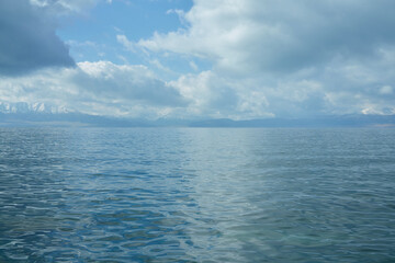 Obraz premium Vast Open Water Under a Dramatic Cloudy Sky with Distant Mountains