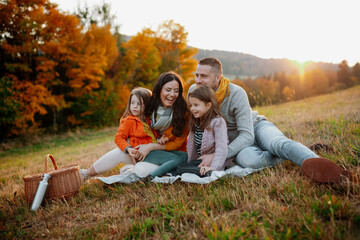 Parents with young children sitting outdoors in autumn light.