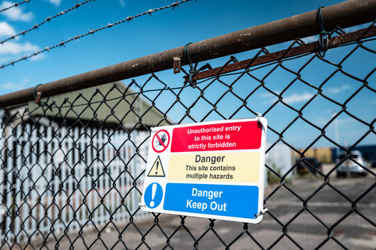 Multiple hazard and no entry seen attached to a rusty fence at the entrance of a factory which produces hazardous chemicals in Britain. The site has strict security.
