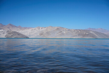 Fototapeta premium Vast Crystal Blue Lake Surrounded by Snowy Mountain Peaks Under a Clear Summer Sky
