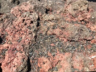 Close-up of bumpy red and grey rock surface with small stones, sunlight shadows forming dramatic natural texture background.
