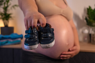Pregnant woman with big belly in anticipation getting ready for the maternity at home. Future mom at 9 months of pregnancy preparing and planning newborn baby boy clothes and shoes