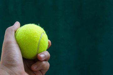 Tennis ball held in hand over dark green background
