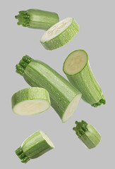 Pieces of fresh zucchinis falling on grey background