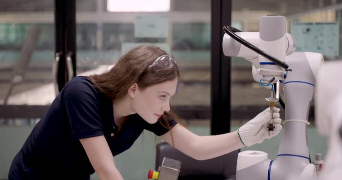 Young female technician slowly calibrating robotic arm in smart robotics lab adjusting component grip during automation training session focused on precise suction control and sensor alignment