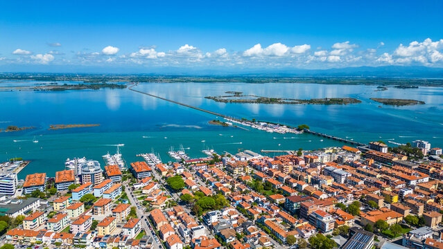 Aerial view of Grado, a picturesque seaside town in Friuli Venezia Giulia, Italy. The photo shows the historic old town with red-tiled roofs, charming harbor, long sandy beaches, blue water