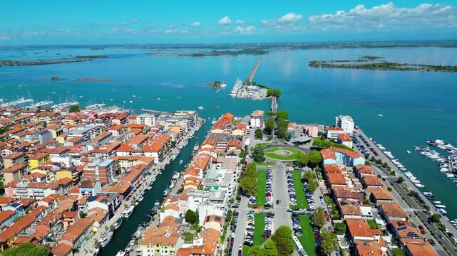 Aerial view of Grado, a picturesque seaside town in Friuli Venezia Giulia, Italy. The photo shows the historic old town with red-tiled roofs, charming harbor, long sandy beaches, blue water