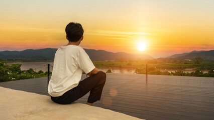 Lonely young man sitting watching the sunset sky