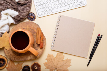 Autumn composition. Office desk with cup of hot tea, empty notebook, keyboard, scarf, dry leaves on beige background. Autumn, fall business concept. Flat lay, top view, copy space