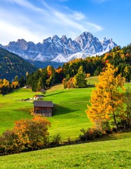 A picturesque autumn landscape showcases rolling hills, vibrant foliage, a rustic wooden barn, and a majestic snow-capped mountain range against a brilliant blue sky.
