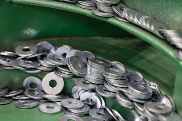 Steel Washers on Vibratory Feeder Track in Industrial Setting. Close-up shot of flat metal washers being oriented on a green vibratory feeder for use in automated assembly. Selected focus