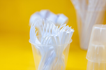 Collection of white plastic forks placed in a transparent cup, photographed in sharp focus with a vivid yellow background, symbolizing disposable utensil use. Selected focus