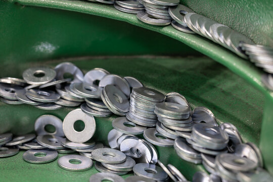 Steel Washers on Vibratory Feeder Track in Industrial Setting. Close-up shot of flat metal washers being oriented on a green vibratory feeder for use in automated assembly. Selected focus