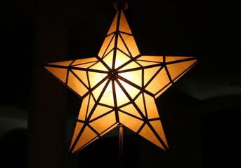 dramatic shot of single parol, geometric filipino christmas star lantern glowing brightly in dark room. festive decoration. symbol of celebration and light. greeting card, banner, holiday.