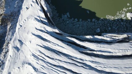 A vertical aerial shot looking down at a cracked glacier and a glacial lake with floating ice chunks and the shadow of a person - Powered by Adobe