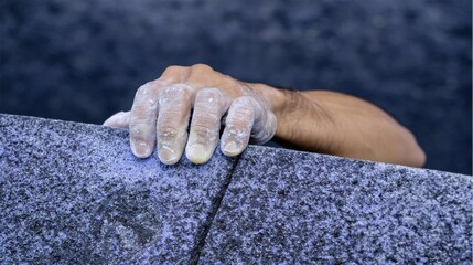 Close up of a climber's hand covered in white chalk gripping a textured blue climbing wall with strength