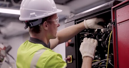 male engineer checks internal electrical components inside automation control cabinet during smart factory maintenance session under industry40 training using gloves and helmet for safety procedures - Powered by Adobe