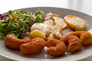 Piatto con gamberi impanati fritti, insalata mista e patate al forno