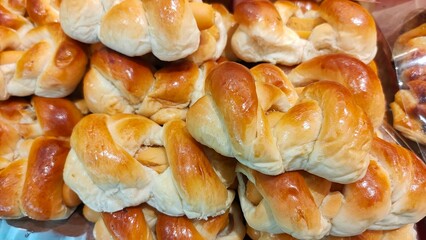 Close-up of golden, braided bread rolls stacked on trays in a bakery display.