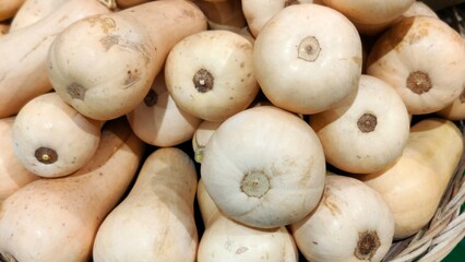 Close-up of a basket piled with pale beige butternut squashes, showing smooth skins and circular stem scars, tightly stacked.