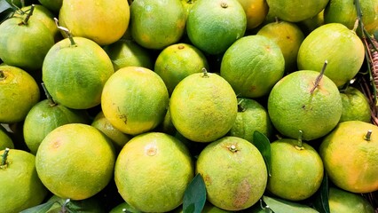 Close-up of a pile of green-yellow citrus fruits with stems and leaves, fresh market produce ready for sale.