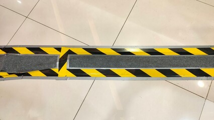 Tiled indoor floor with black-and-yellow striped hazard tape covering a recessed cable channel or...